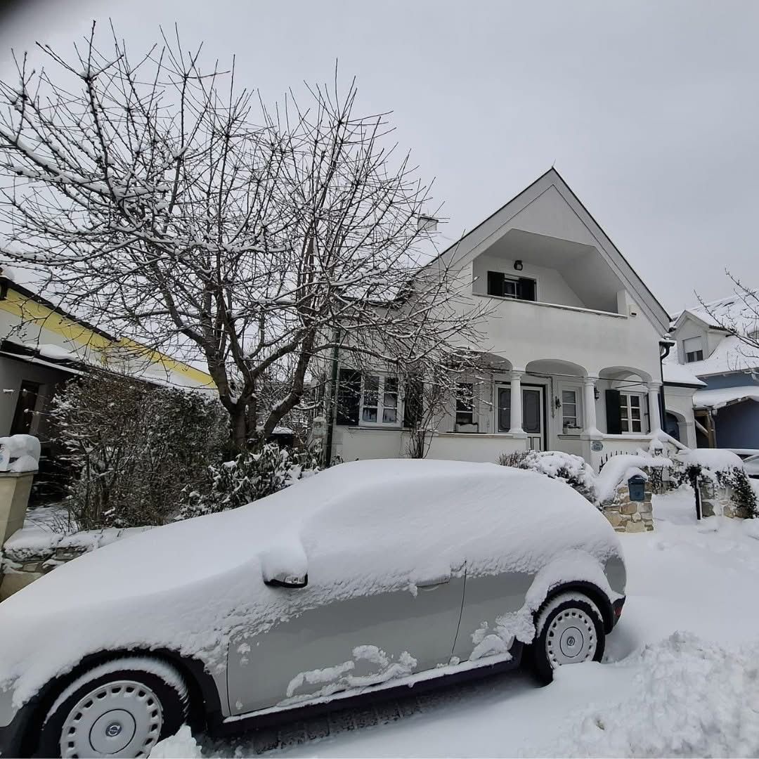 Ein silbernes Auto, das in Schnee bedeckt ist, steht vor einem Haus mit schneebedecktem Dach und Balkon.
