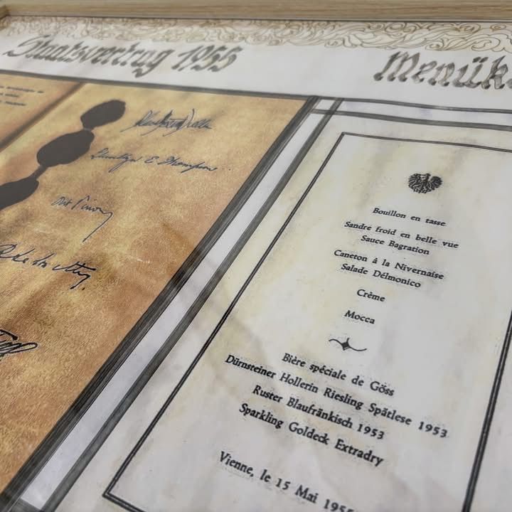 Ein altes Menü von 1953, auf einem Tisch mit einem braunen Papierhintergrund platziert. Es hat handgeschriebene Notizen und ist in einem goldfarbenen Rahmen eingefasst.