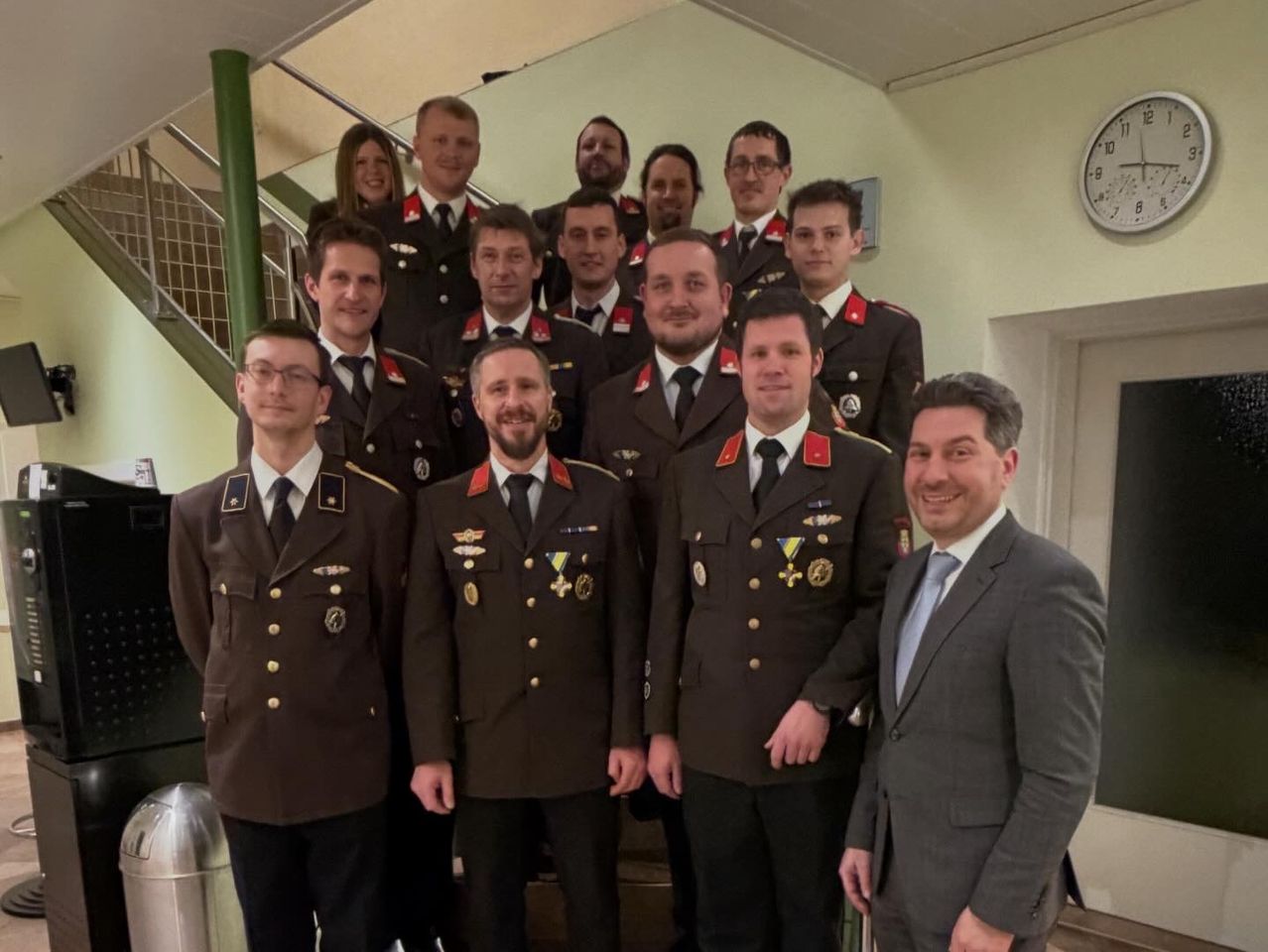 Eine Gruppe uniformierter Militärangehöriger posiert für ein Foto, mit einem lächelnden Mann in Anzug, der rechts steht.