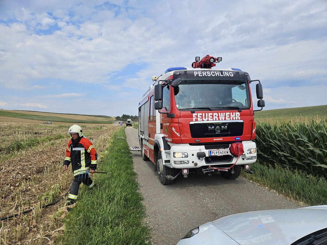 Feuerwehrmann mit Schaufel und Feuerwehrauto in Perschling vor einem Maisfeld