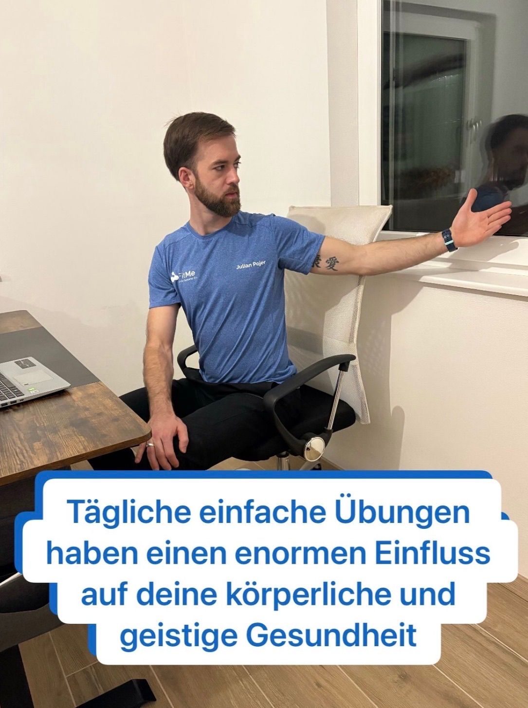 A man sits at a desk in an office, gesturing with his arm while wearing a blue shirt. A laptop is on the desk, and he appears to be addressing someone outside the window.