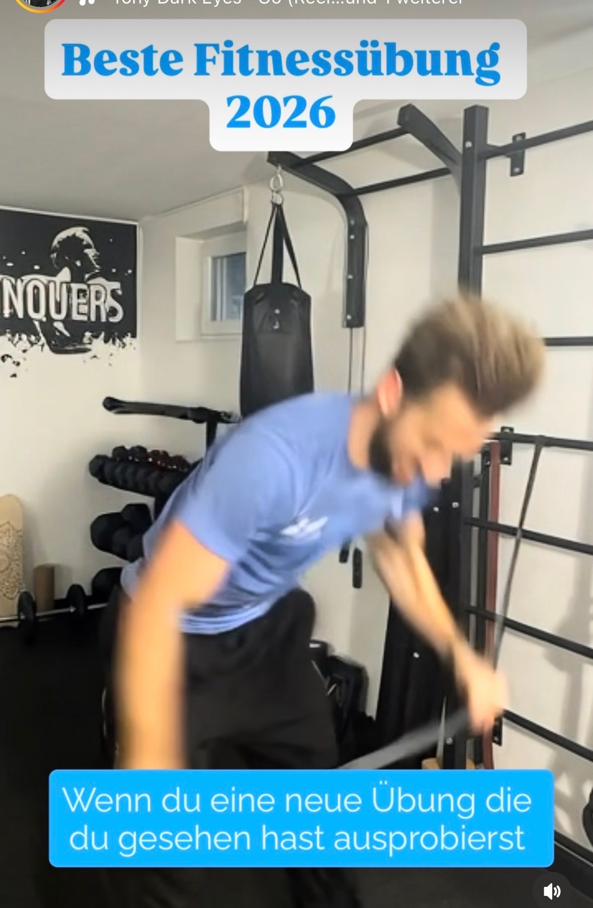 A man in a blue shirt and black pants is exercising in a gym, holding a metal bar with both hands.