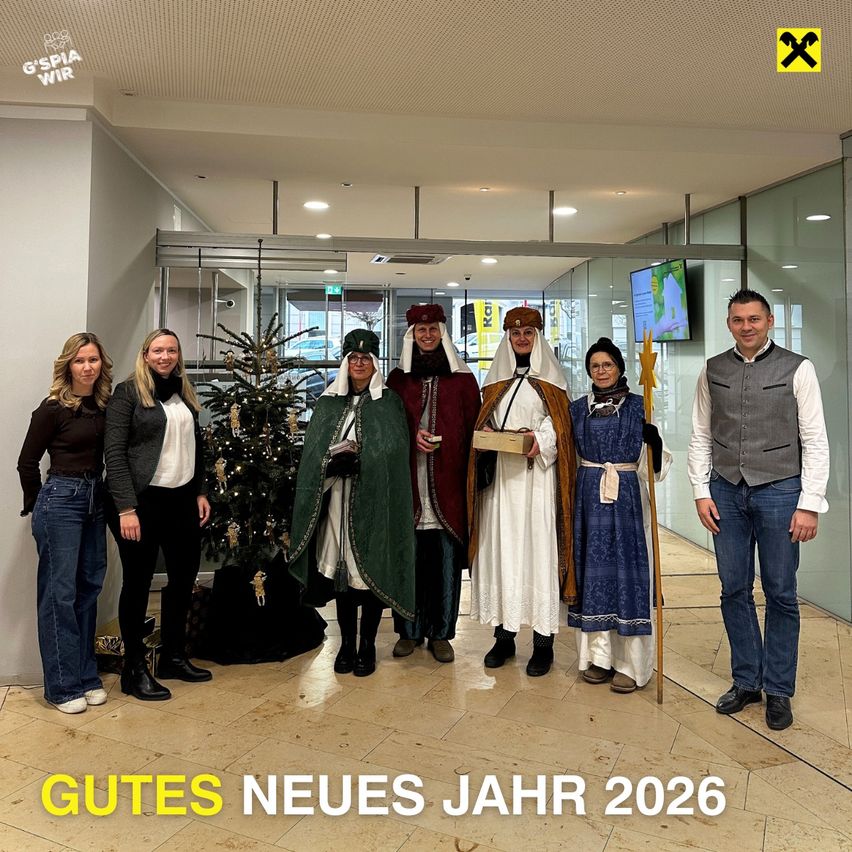 Gruppenfoto mit Kollegen in festlicher Kleidung; ein Weihnachtsbaum im Hintergrund; die Nachricht lautet 'GUTES NEUES JAHR 2026'.