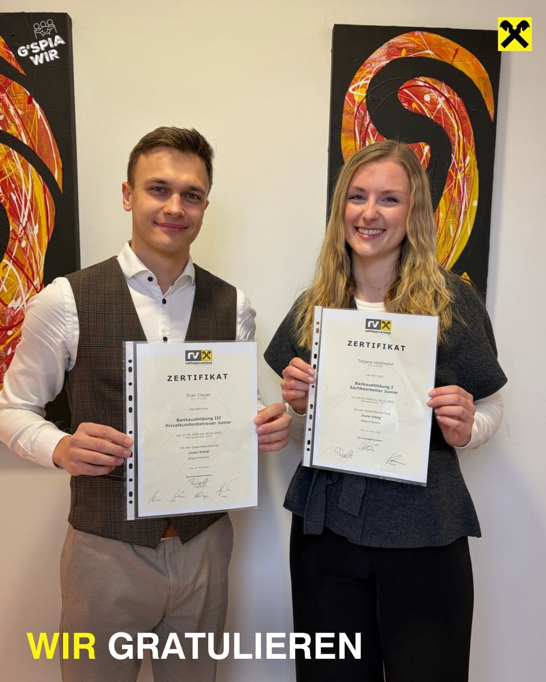 Two individuals stand in front of a white wall with abstract paintings, holding certificates. The man on the left wears a vest over a white shirt, and the woman on the right holds her certificate. Both look happy.