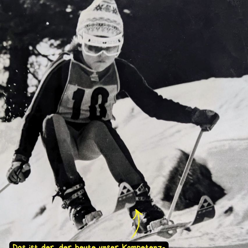 A skier in a black and white ski suit with a number 18, skiing downhill with a yellow arrow pointing to the ski boots.