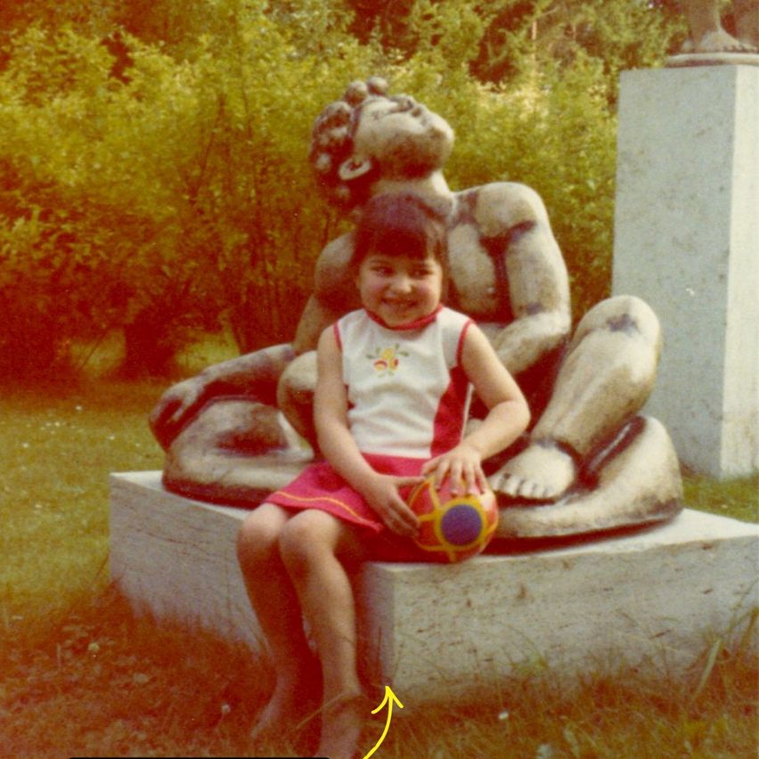 A girl sits on a concrete block, holding a ball. She is smiling and looking forward, with a statue behind her.
