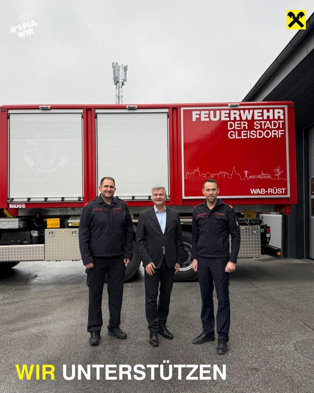 Three men stand in front of a red fire truck with the words 'Feuerwehr der Stadt Gleisdorf' on it. They are dressed in black uniforms and suits.