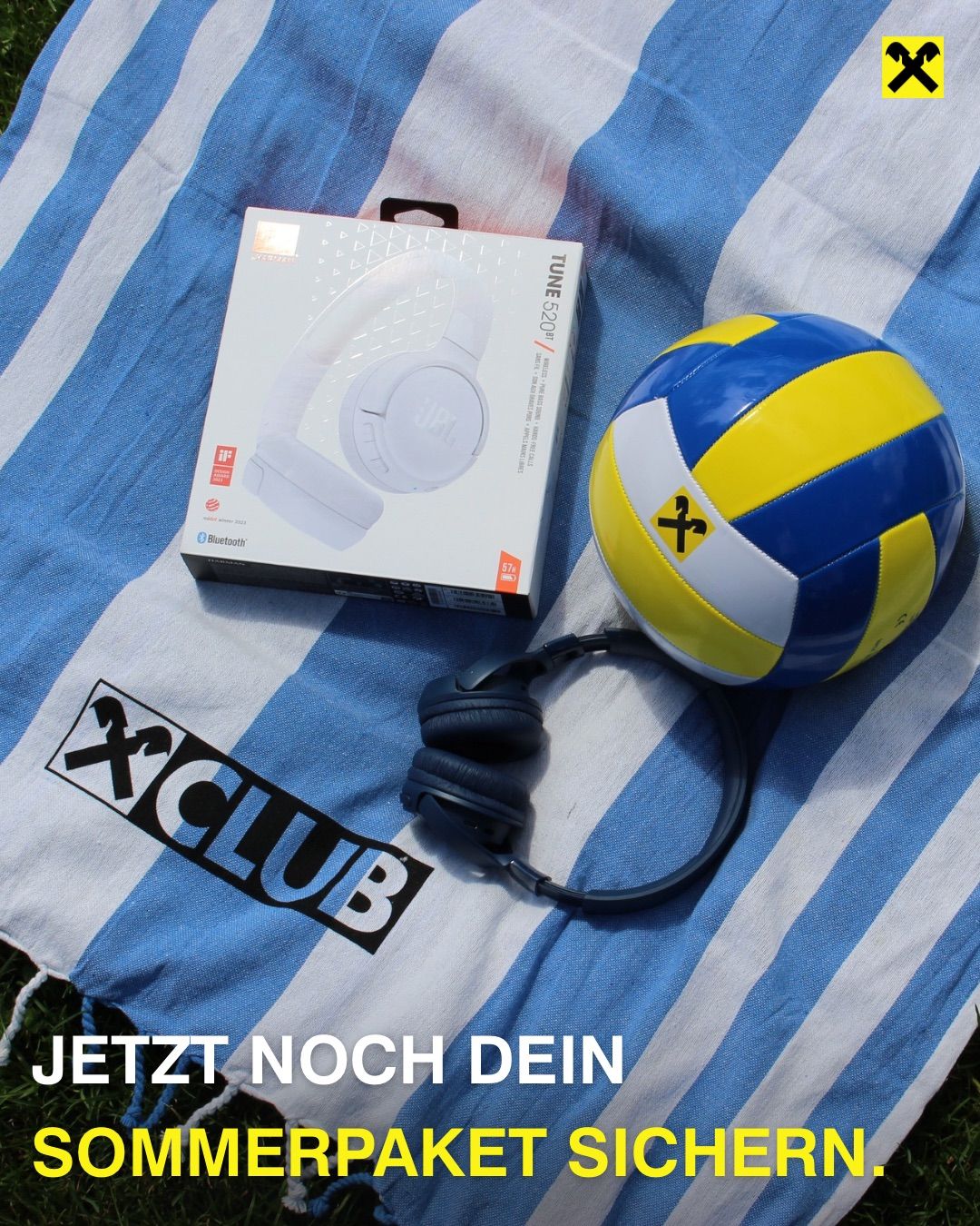 Eine JBL Tune 520BT Kopfhörerbox, ein Volleyball und ein Handtuch mit dem Text 'JETZT NOCH DEIN' darauf.