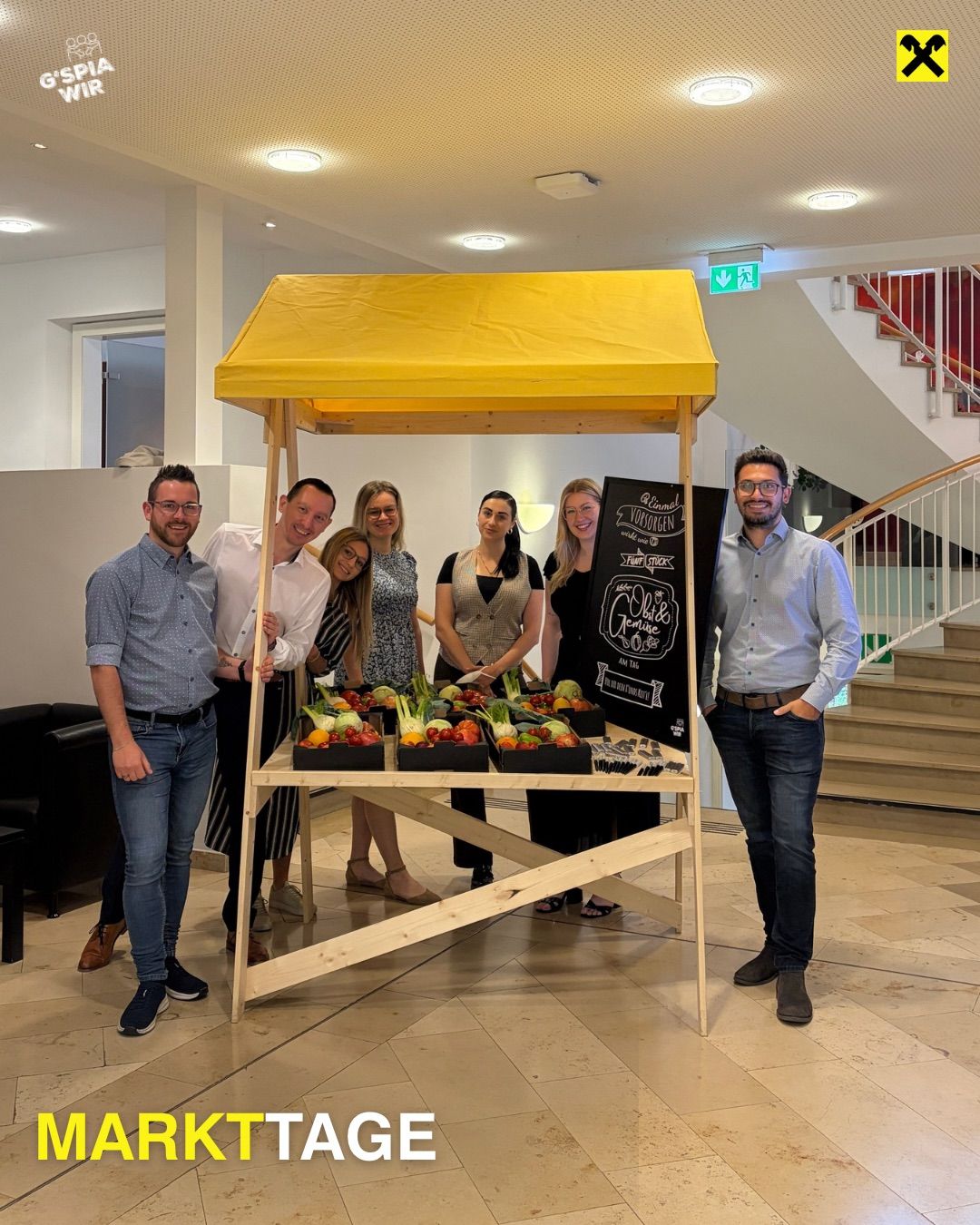 Eine Gruppe von Menschen steht hinter einem kleinen gelben Zelt voller Gemüse. Sie posieren für ein Foto mit einer Tafel, auf der 'Vogelgen' steht.