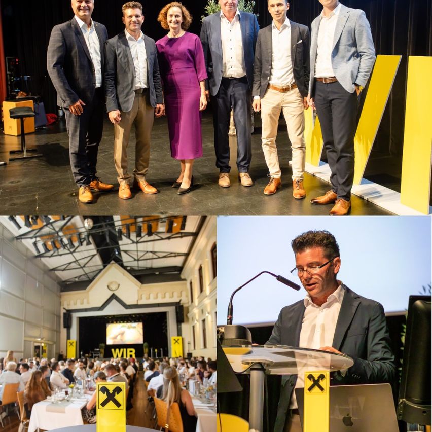 Eine Gruppe von Fachleuten in Anzügen und einer Frau in einem lila Kleid stehen auf der Bühne. Unten spricht ein Mann an einem Podium während einer Konferenz.