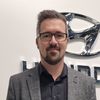 Ein Mann mit Brille und grauem Jackett steht vor einem Hyundai-Logo an einer weißen Wand.