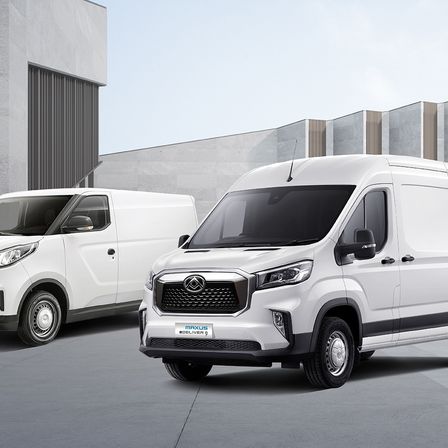 Zwei weiße Lieferwagen stehen vor einem Gebäude. Der vordere Lieferwagen hat ein 'Maxus Deliver 9'-Schild am Stoßfänger.