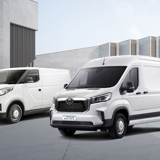 Zwei weiße Lieferwagen stehen vor einem Gebäude. Der vordere Lieferwagen hat ein 'Maxus Deliver 9'-Schild am Stoßfänger.