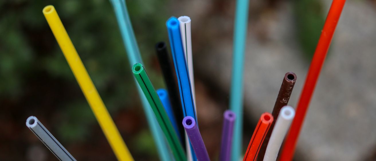 Eine Nahaufnahme verschiedener farbiger Plastikstrohhalme und Röhren, einschließlich Blau, Gelb, Grün und Rot. Der Hintergrund ist unscharf mit einer Mischung aus Grün- und Brauntönen.
