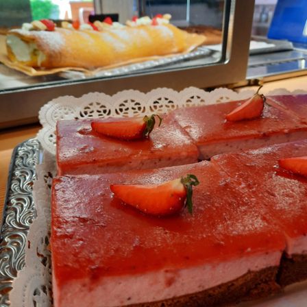 Ein Nahaufnahme einer Erdbeertarte mit einer weißen Spitzenunterlage, mit einem gelben Kuchen und einem blauen Stuhl im Hintergrund sichtbar.