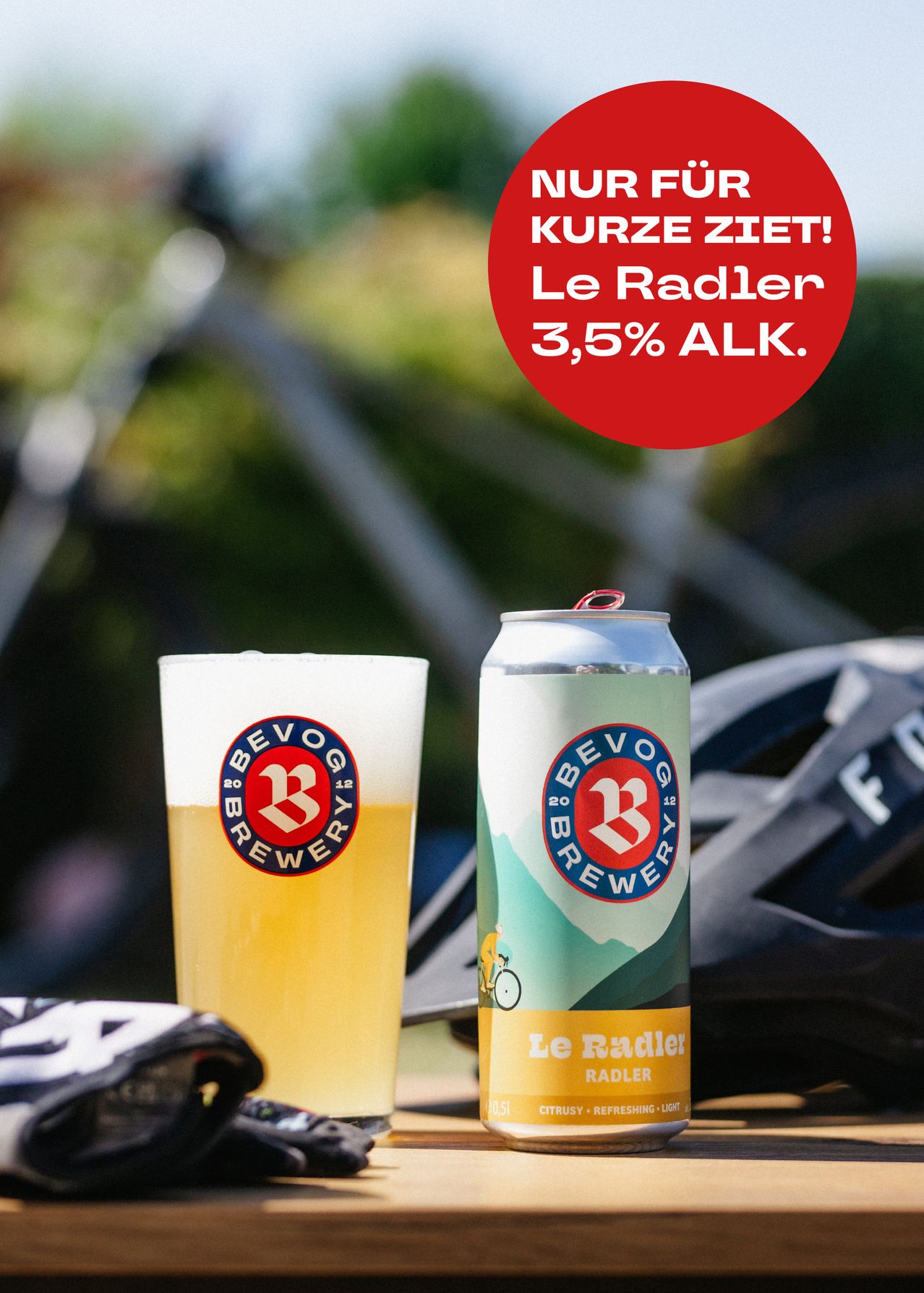 Ein Glas und eine Dose Le Radler Bier mit 3,5% Alkoholgehalt. Der Hintergrund ist unscharf mit einem Fahrrad und Helm.