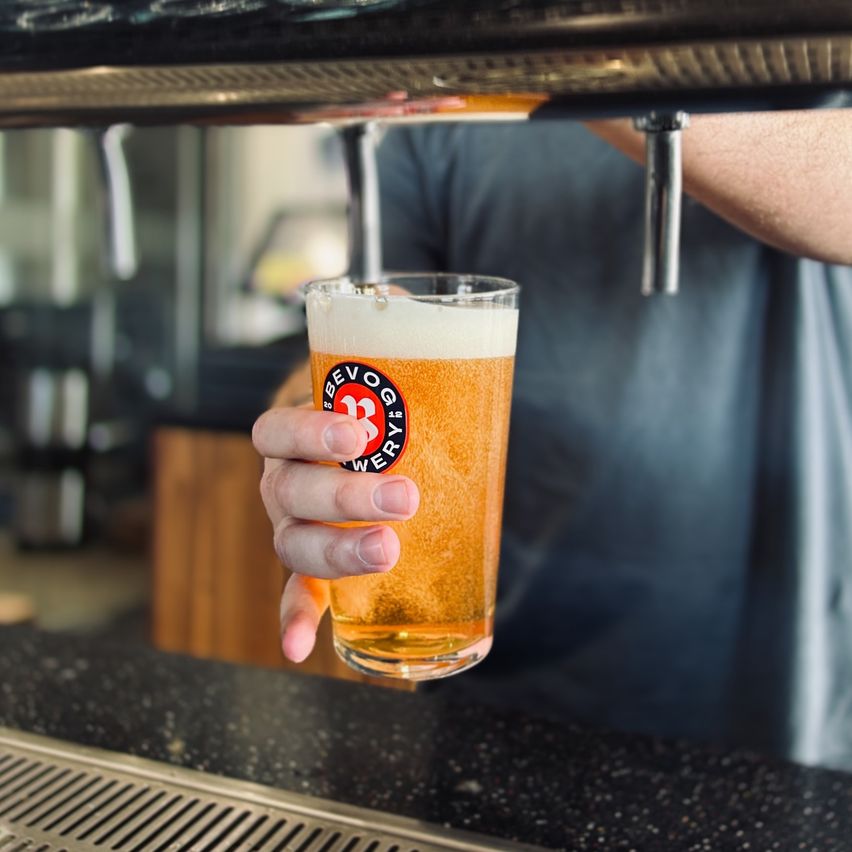 Ein Barkeeper hält ein Glas Bier, das mit einem Logo für Bevog Brauerei gekennzeichnet ist.