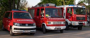 Drei Feuerwehrfahrzeuge sind auf einem Parkplatz geparkt. Zwei der Fahrzeuge sind rot und weiß und eines ist weiß. Das Wort 'FEUERWEHR' steht auf der Front der roten Fahrzeuge.