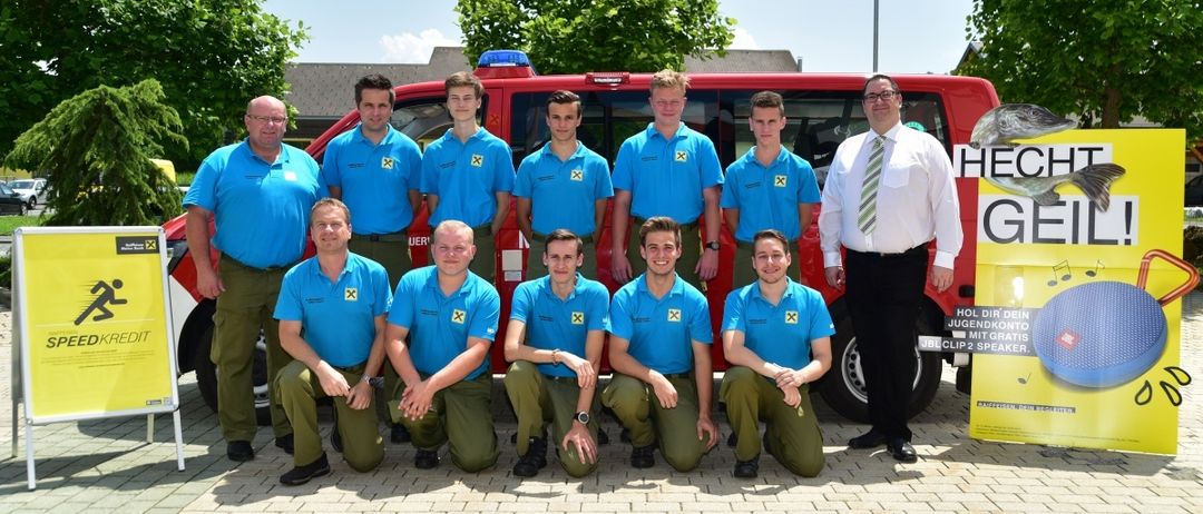 Eine Gruppe junger Männer in blauen Uniformen posiert für ein Foto vor einem roten Fahrzeug mit einem Mann in weißem Hemd und Krawatte.