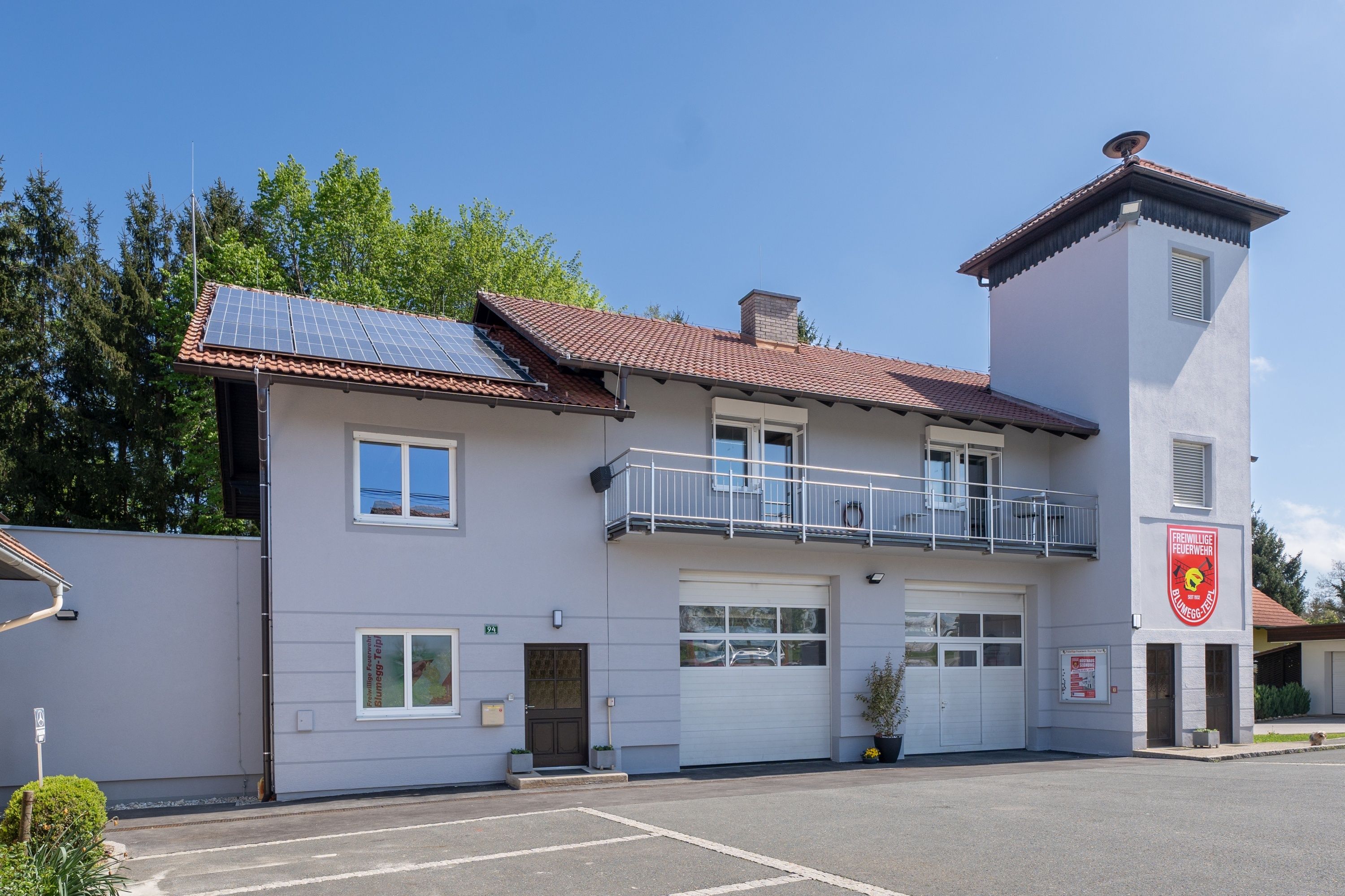 Ein zweistöckiges Haus mit Solarpanelen auf dem Dach. Es hat drei Fenster und zwei Garagen. Bäume sind hinter dem Haus sichtbar.