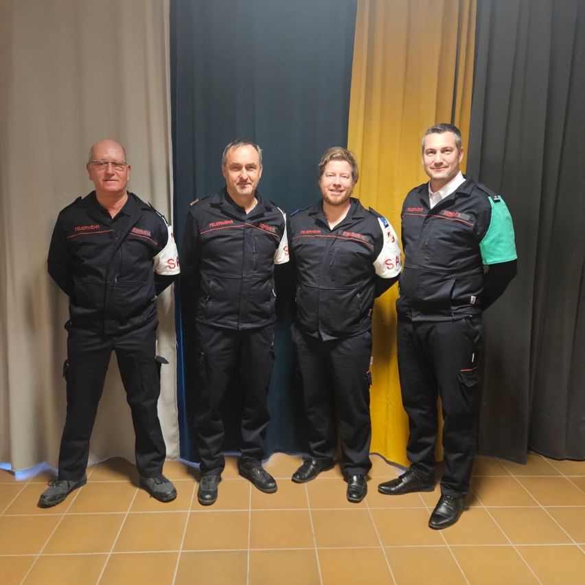 Vier Männer in Uniform stehen nebeneinander. Sie lächeln und scheinen für ein Foto zu posieren.