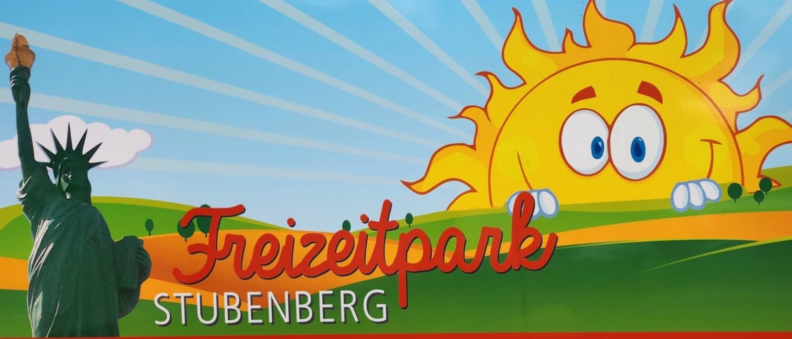 Eine fröhliche Sonne lächelt hell über eine Landschaft mit den Worten Freizeitpark Ubenberg auf einem blauen Himmelshintergrund.