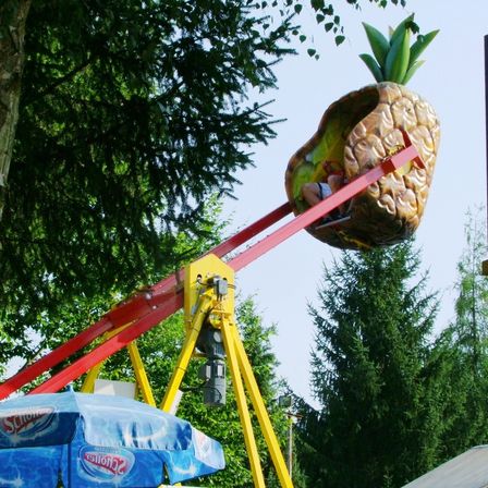 Eine Person fährt auf einer rot-gelben Achterbahn mit Ananas-Thematik, unter einem blauen Schirm mit dem Corona-Logo.
