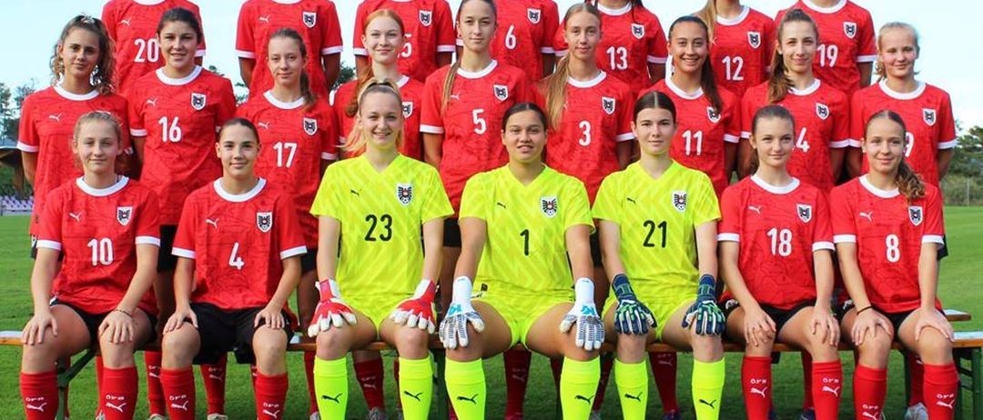 Eine Fußballmannschaft in roten und gelben Trikots posiert für ein Gruppenfoto auf einem grünen Feld. Die Spieler tragen Handschuhe und Turnschuhe.