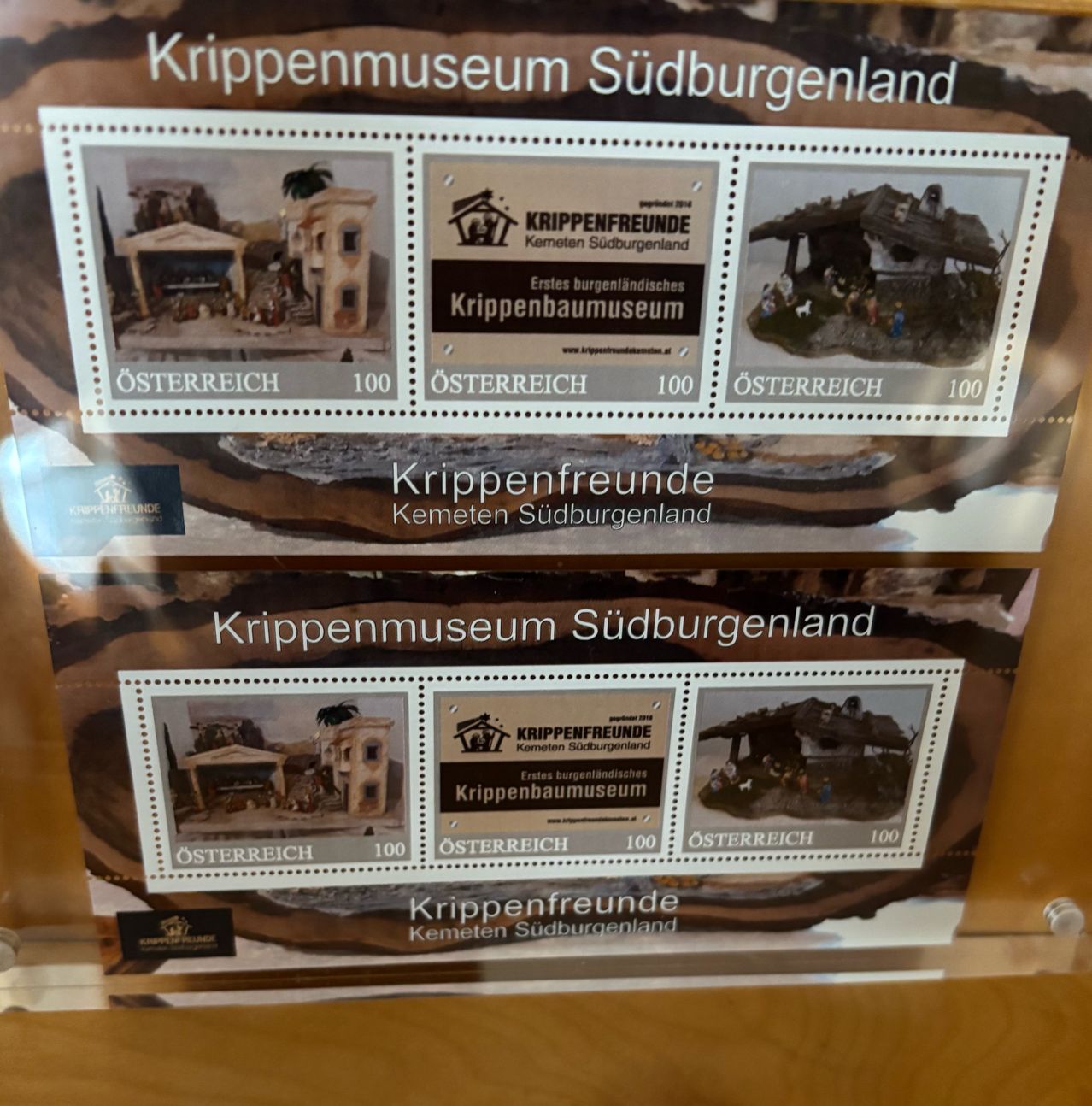 Display of Austrian stamps related to Krippenmuseum, with images of nativity scenes and the museum logo, presented on a wooden surface.