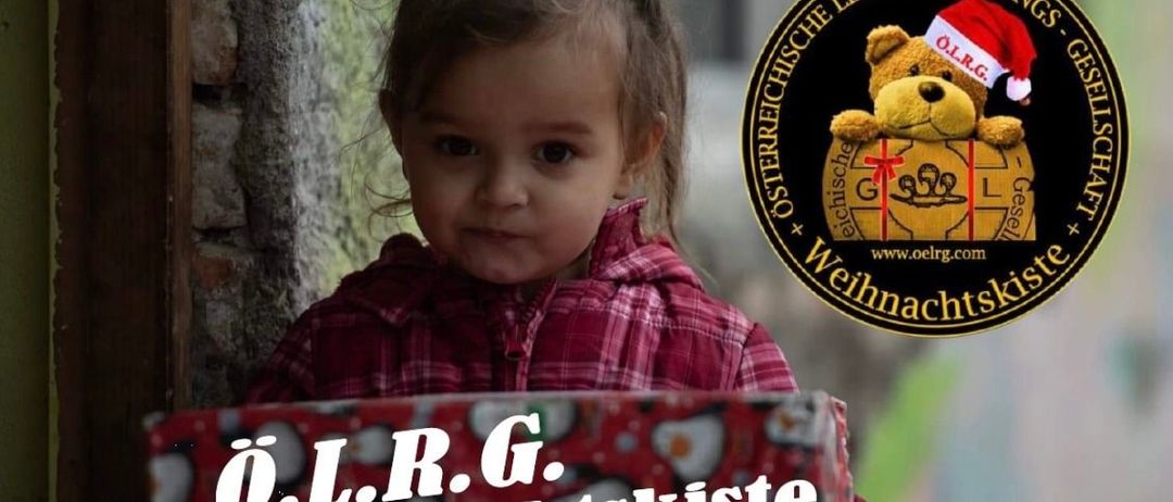 Ein junges Mädchen, das einen Weihnachtshut trägt, hält eine Weihnachtsgeschenkbox. Auf der Box steht der Text 'O.L.R.G. Weihnachtskiste'. Es gibt ein Logo mit einem Teddybären und einer Website-URL.