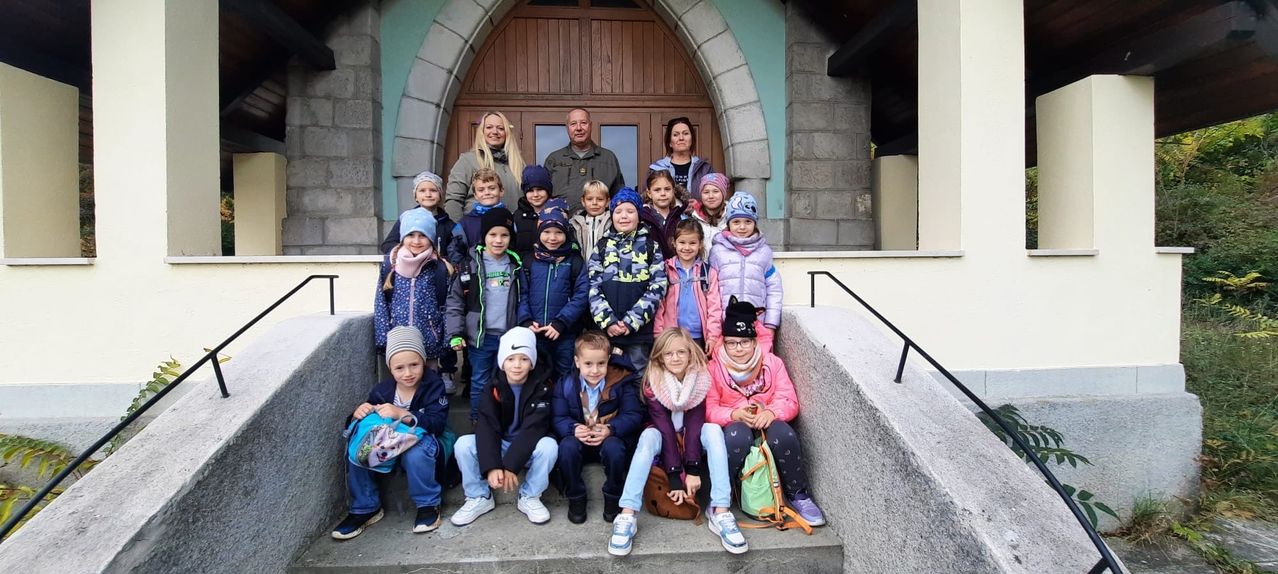 Eine Gruppe von Kindern, Erwachsenen und Lehrern posiert für ein Foto vor einer Kirche, wobei ein Erwachsener im Hintergrund steht.