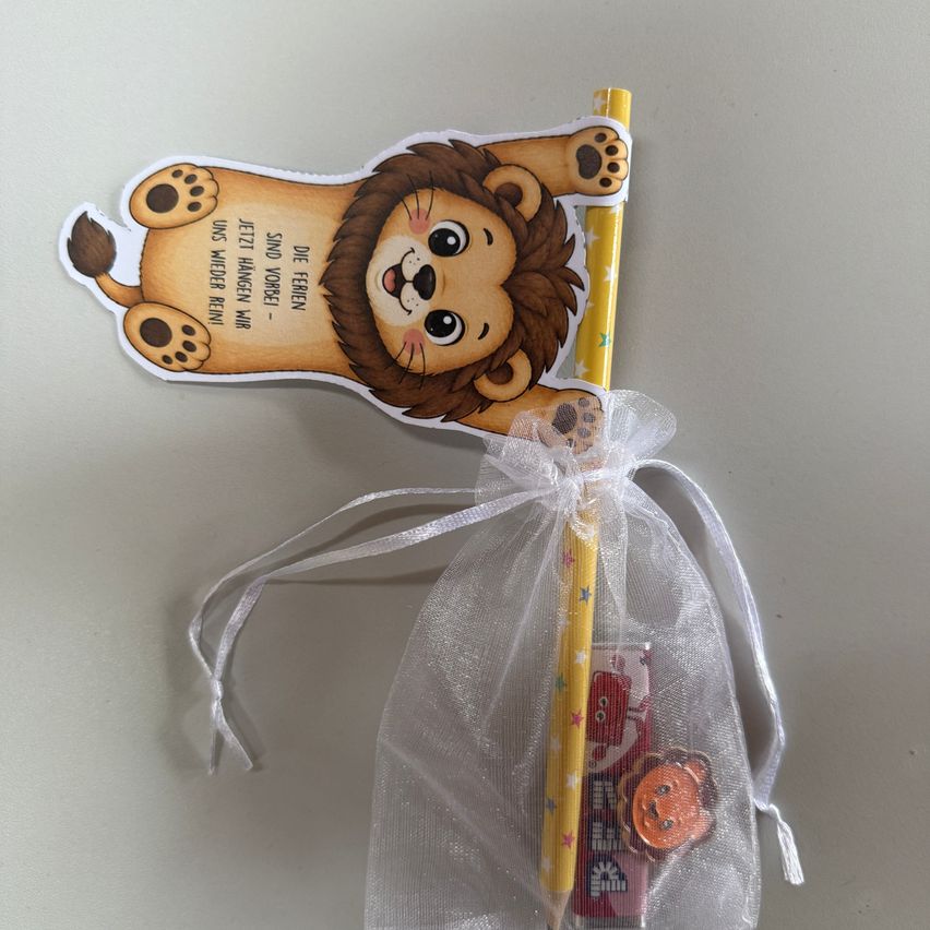 Ein gelber Stift mit einem Löwenaufkleber und einer kleinen Tüte mit Süßigkeiten, die mit einem Band befestigt ist. Der Löwenaufkleber hat einen deutschen Satz darauf.