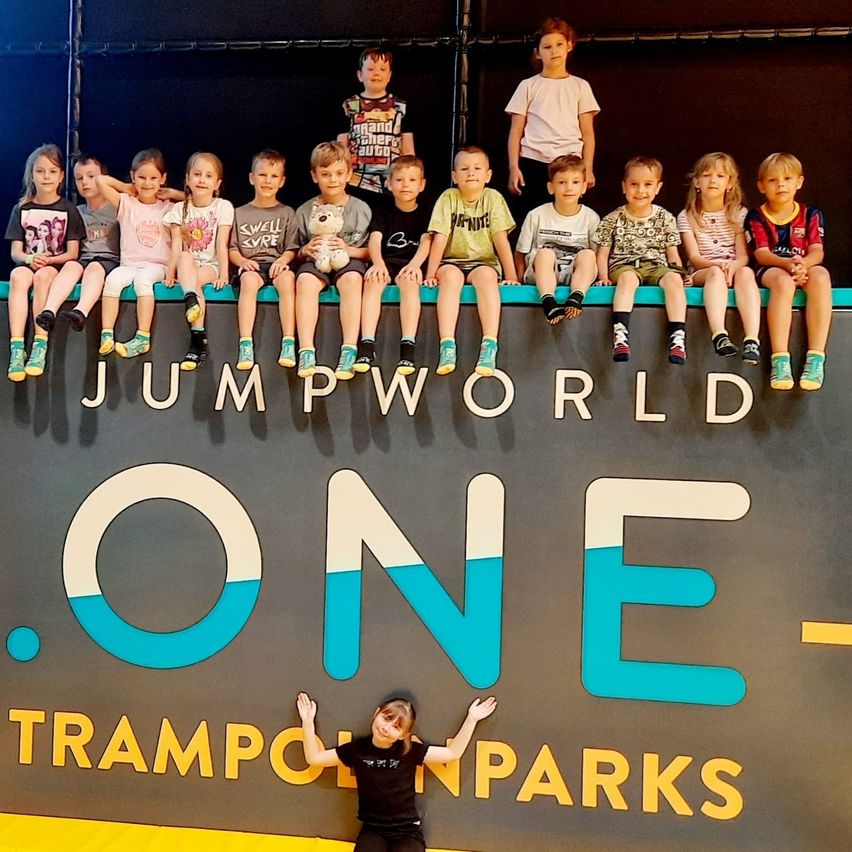 Eine Gruppe von Kindern in Sportbekleidung posiert auf einem Jump World Trampolinpark-Schild. Ein Kind kauert unten.