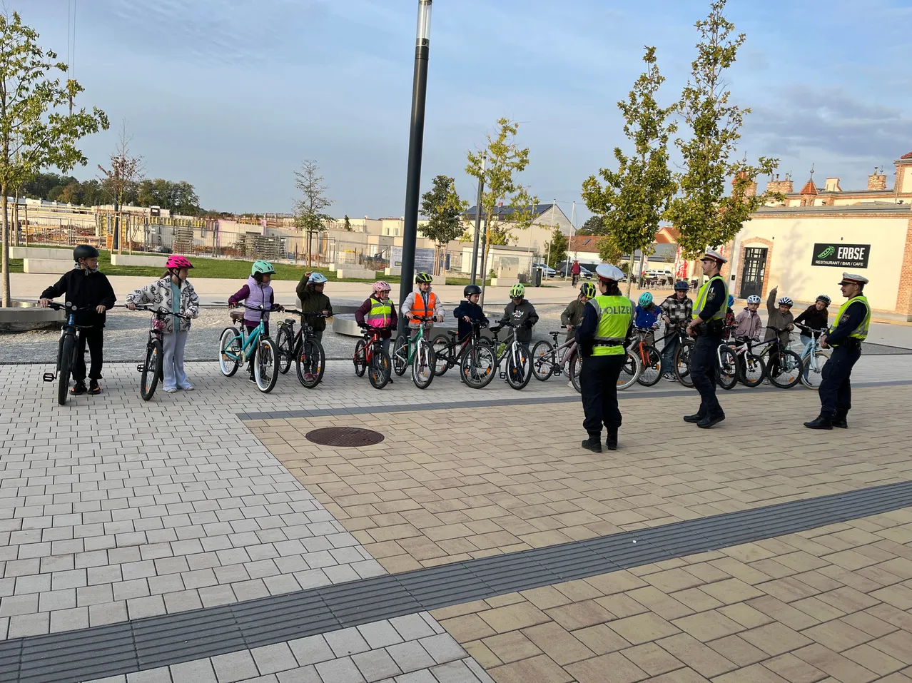 Polizei-Schulung: Kinder mit Fahrrädern und Polizisten in Uniform stehen auf einem Platz.