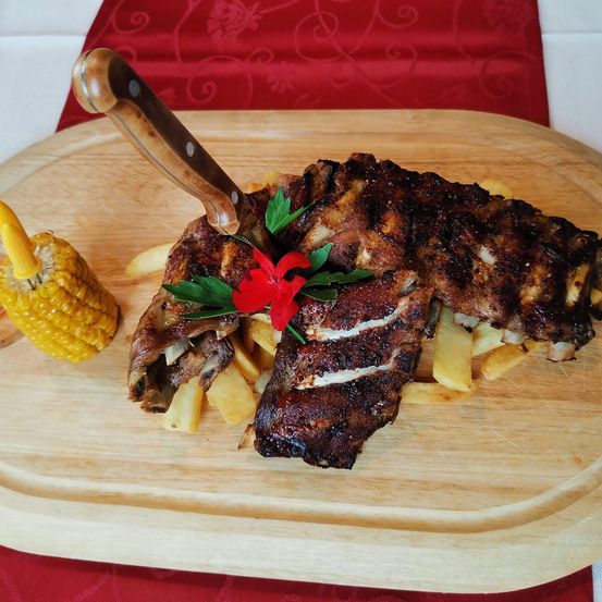Gegrillte Rippchen mit einer roten Blume und Mais auf einem Holzbrett.
