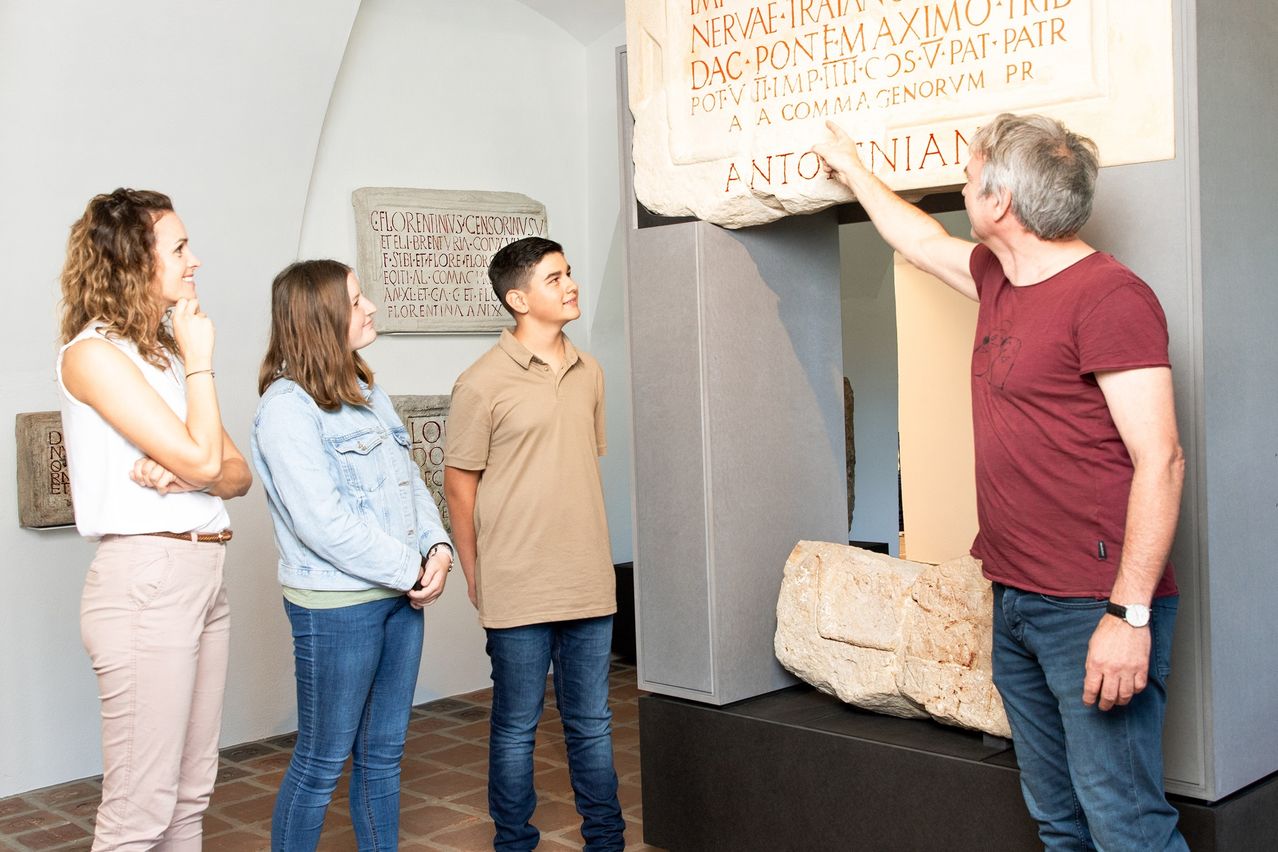 A man points to an ancient stone inscription while a woman and boy look on, showcasing an indoor exhibit.