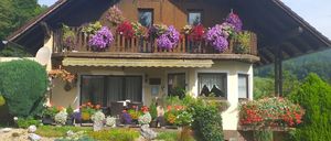 Ein gemütliches Haus mit Balkon und Markise, umgeben von einem Garten voller bunter Blumen und Grünpflanzen.