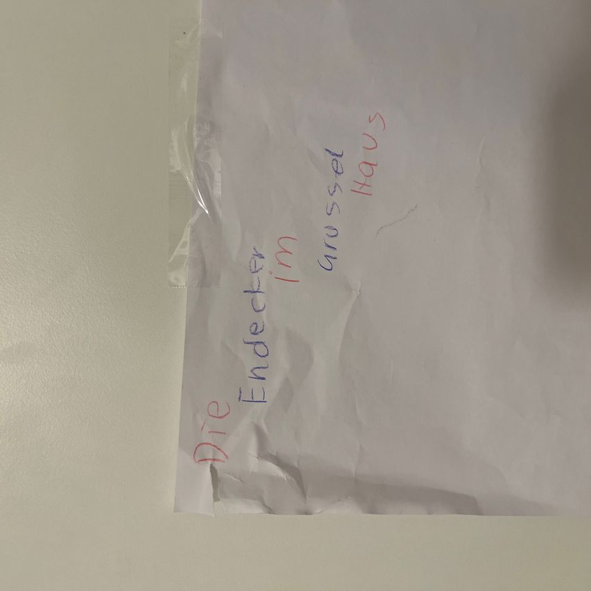 A crumpled white paper with red and blue writing on it. The words are 'Die Endloser' and 'in Wachstum Haus'. The paper is folded and has a slightly torn edge.