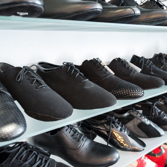 Ein Regal gefüllt mit verschiedenen schwarzen Lederschuhen, einschließlich Schnürschuhe, Slip-Ons und Business-Schuhe, ordentlich angeordnet.