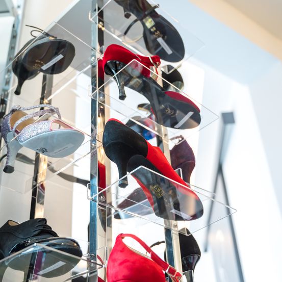 Eine Ausstellung verschiedener High-Heel-Schuhe in klaren Vitrinen, einschließlich roter, schwarzer und silberner Schuhe, vor einem weißen Wandhintergrund.