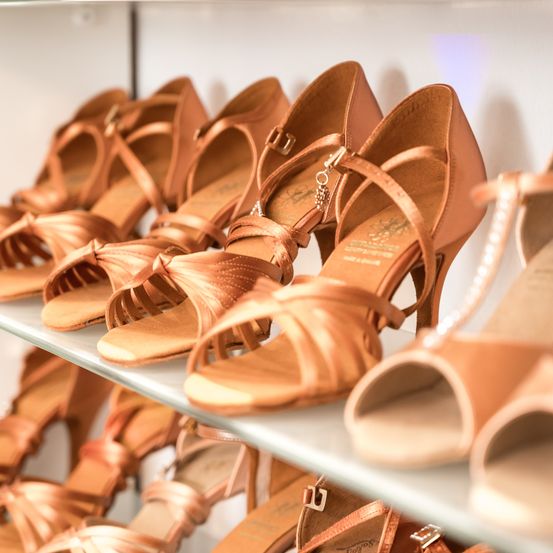 Eine Sammlung von rosegoldfarbenen hochhackigen Sandalen ordentlich auf einem Ausstellungsregal angeordnet. Die Schuhe sind mit dekorativen Elementen verziert.