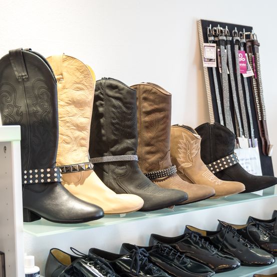 Eine Präsentation von Cowboy-Stiefeln und Ledergürteln auf einem Regal. Verschiedene Farben und Designs werden präsentiert.
