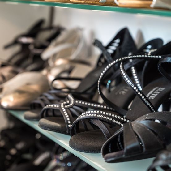 Eine Nahaufnahme eines Glasregals mit mehreren Paaren schwarzer Damensandalen mit dekorativen Kristalldetails.