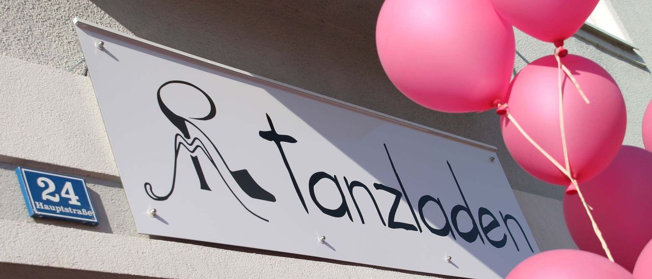 Ein Ladenschild für Tanzladen mit einem Schuhsymbol und rosa Luftballons darüber.
