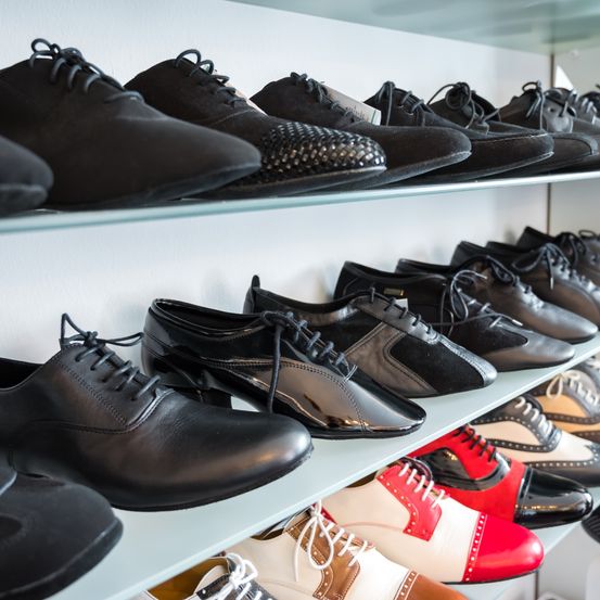 Eine Sammlung von formellen Schuhen auf einem Regal, einschließlich schwarzer, roter, weißer und brauner Lederschuhe.