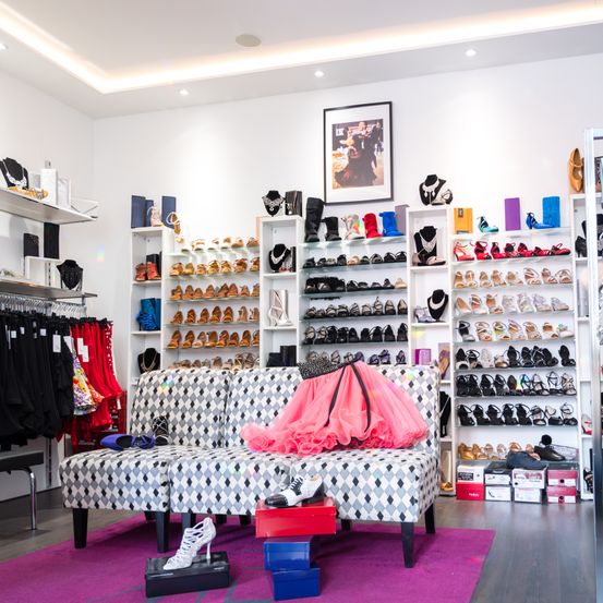 Ein Boutique-Laden mit weißen Wänden und Regalen voller Schuhe, einem Sofa mit einem rosa Tutu und Schmuck.