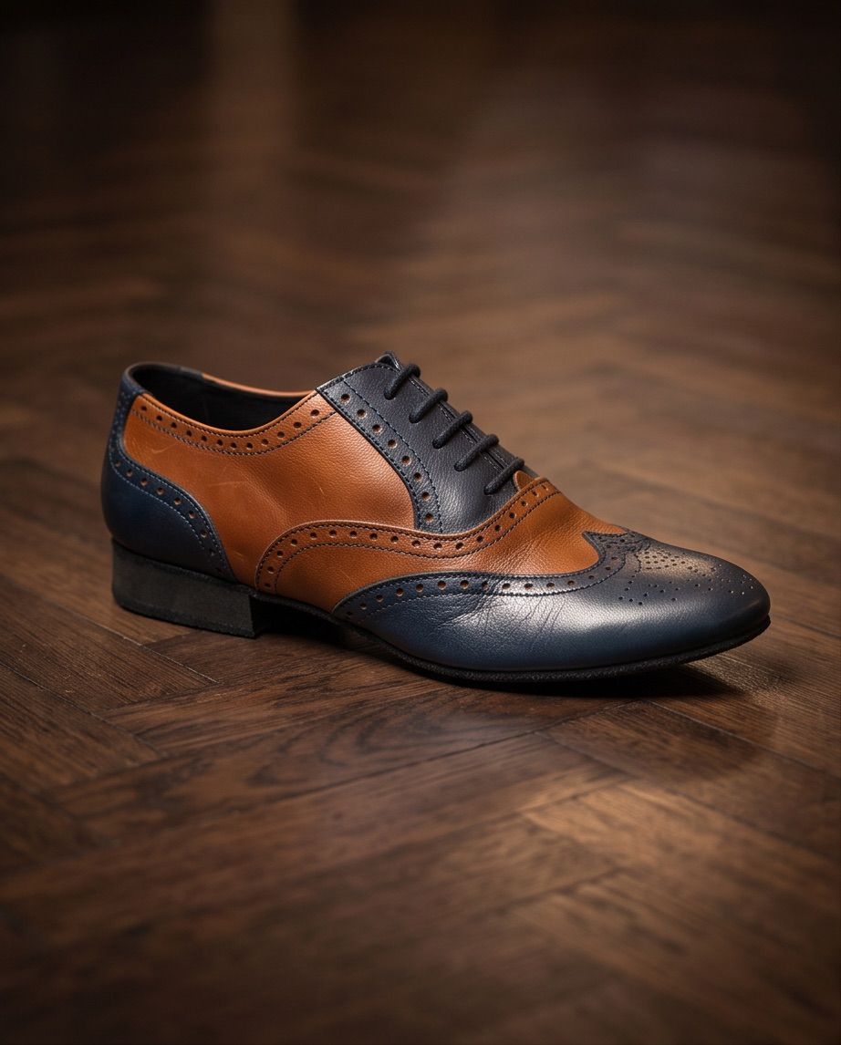 Ein navyblauer und brauner Leder-Wingtip-Schnürer mit schwarzer Sohle und Schnürsenkeln auf einem Holzboden.