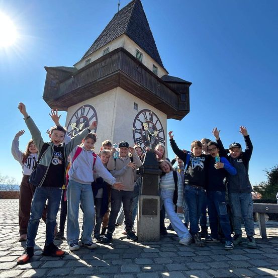 Eine Gruppe von Kindern und Jugendlichen steht vor einem Uhrenturm und posiert für ein Foto.