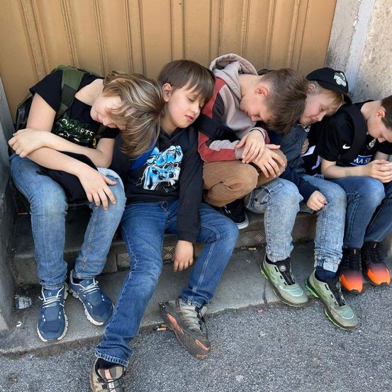 Fünf junge Jungen sitzen auf den Stufen und schlafen alle. Ein Junge hat seinen Kopf auf der Schulter eines anderen Jungen.