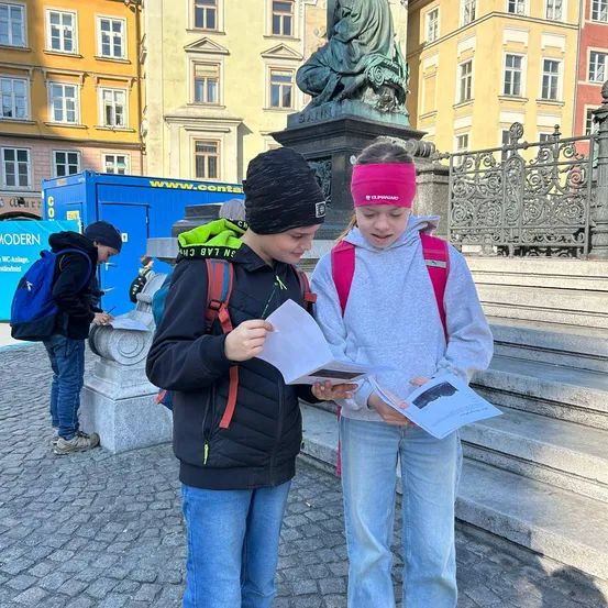 Zwei Kinder mit Rucksäcken betrachten eine Karte auf dem Alten Stadtplatz in Warschau, Polen.